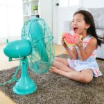 a girl sitting in front of table fan