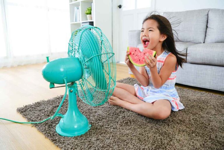 a girl sitting in front of table fan
