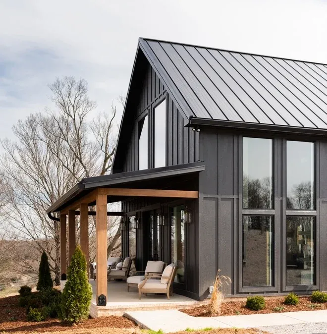 A black house and with wooden overhang and chair outside the house and black framed windows