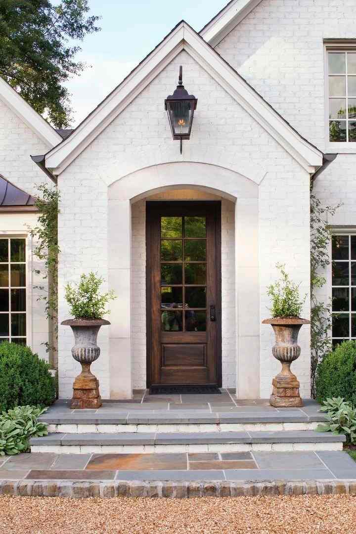 A brick pathway and two pots placed on each side of the door and the light above the door