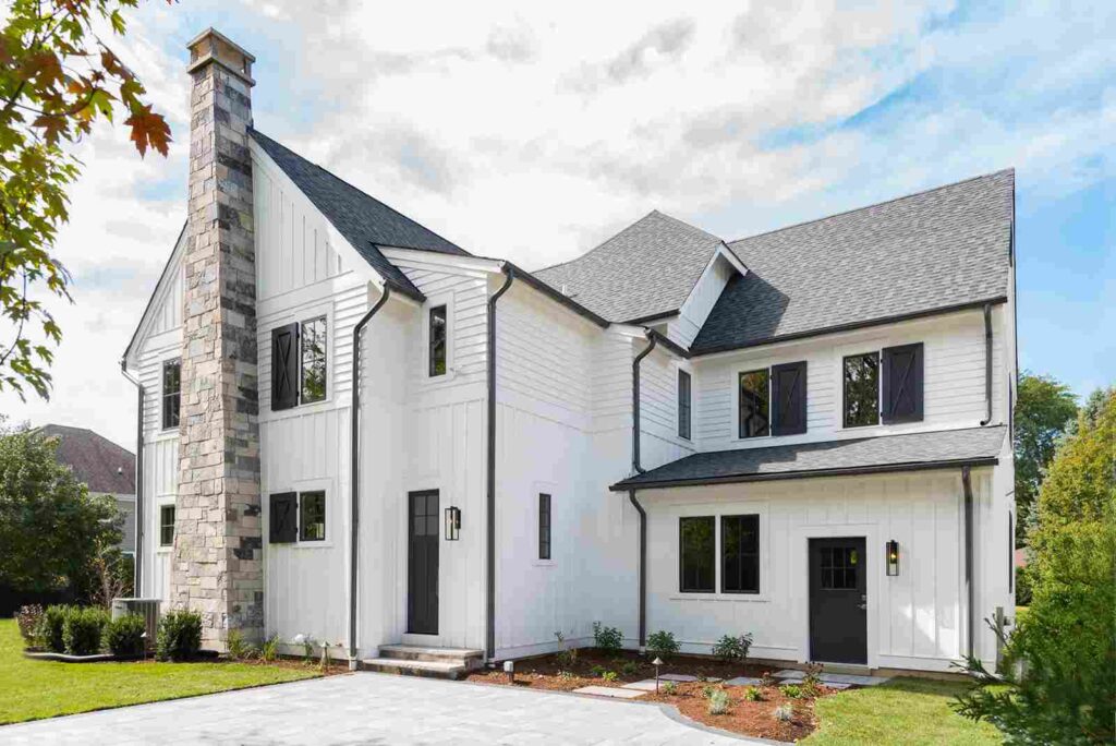 A white house with black gutter and window and some plants outside of the house and celling light on the wall
