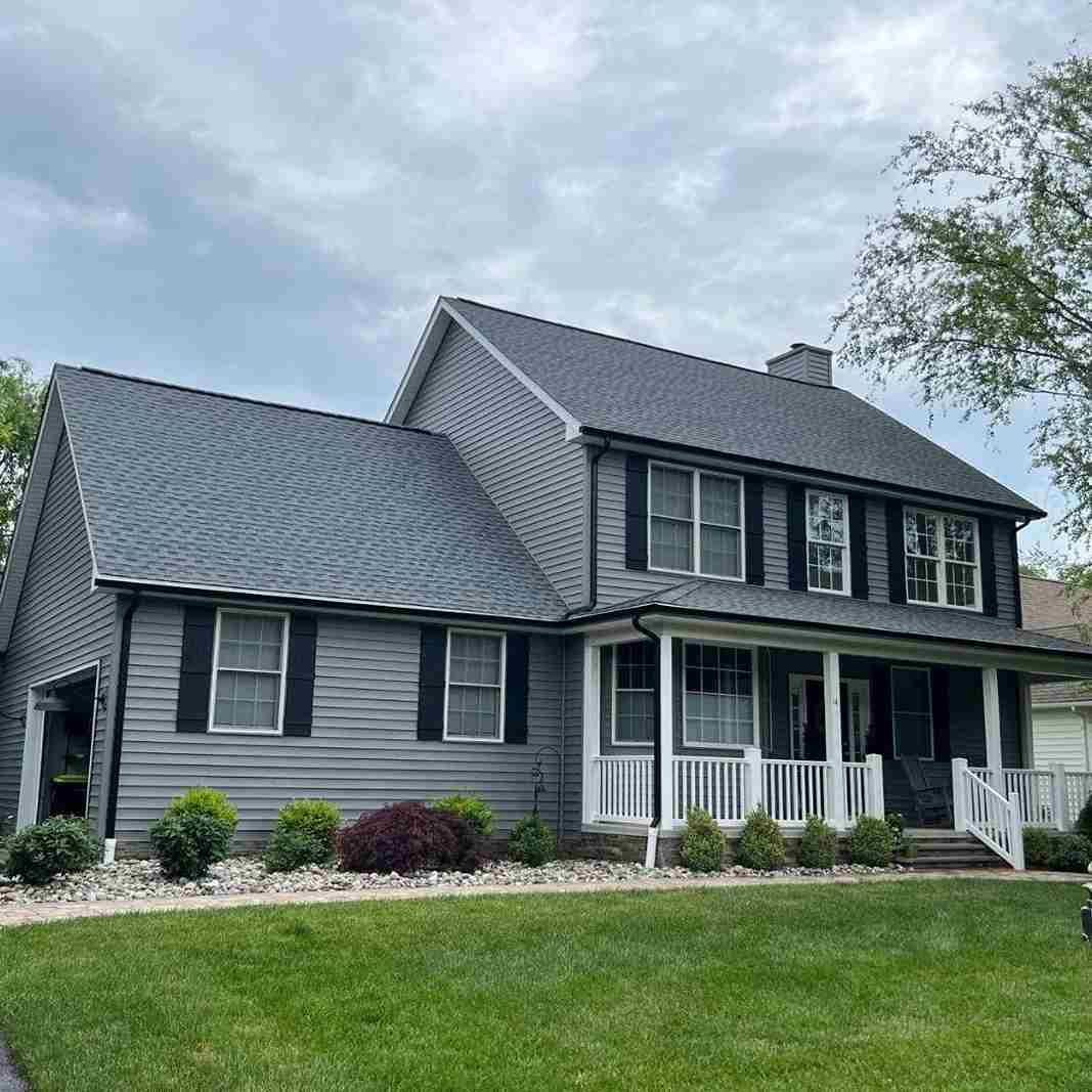 A white trim window and gray house and black gutter and garden outside of the house