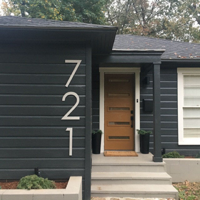 A black house and wooden front door and black roof and numbers on the wall