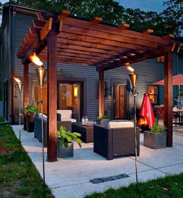 A black house and wooden pergola and sofa and table and plants on the floor