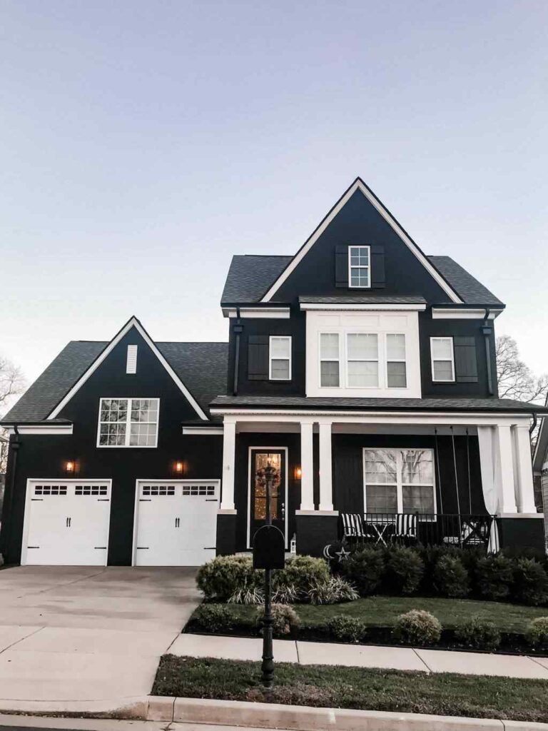 A black house and white trim and white framed windows and white pillars and garden outside of the house