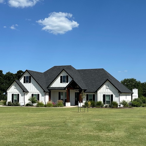 A black matter roof and white house and white trim window and garden outside of the house
