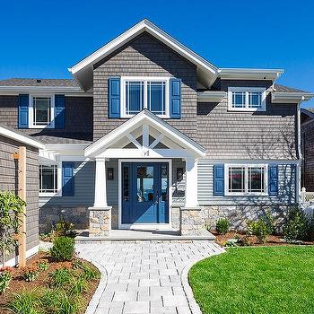 A gray house with blue shutter and garden on each side and a stone pathway