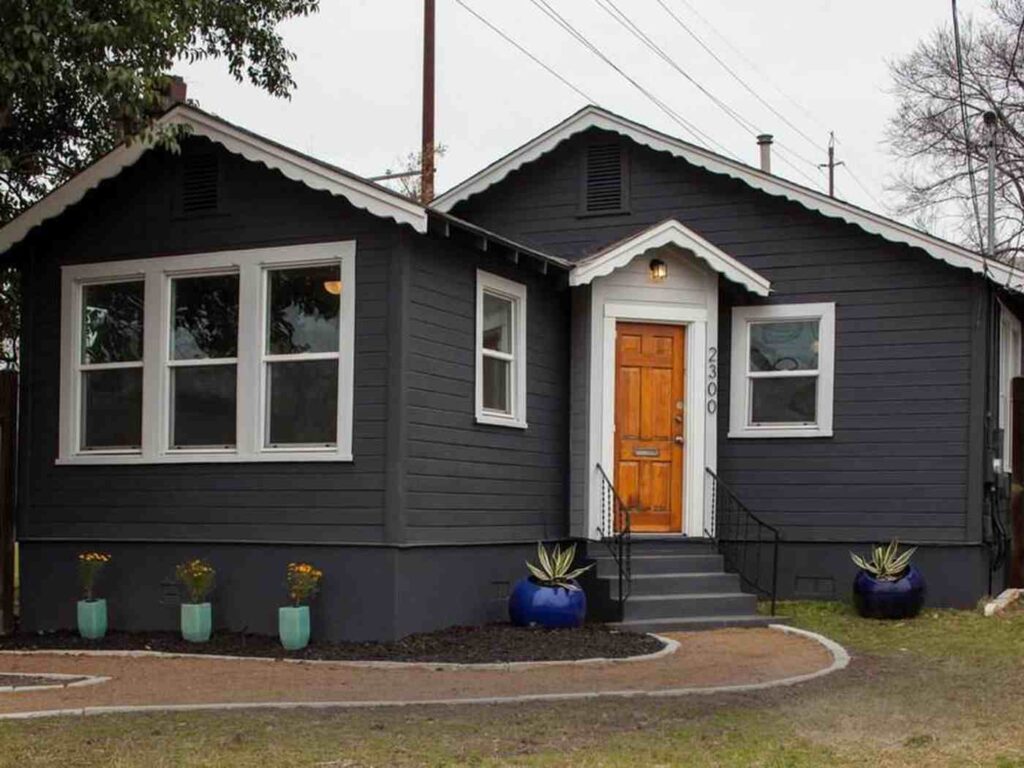 A dark house and white trim roof and wooden stain door and plotted plants each side on the house