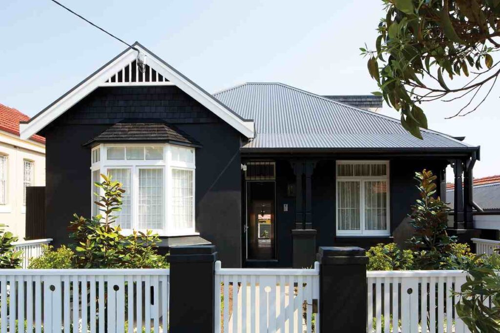 A black house with gable roof and white fencing around the house and glass door