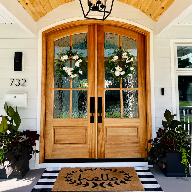 A wooden glass stain door and plants on each side of the door and mat on the floor