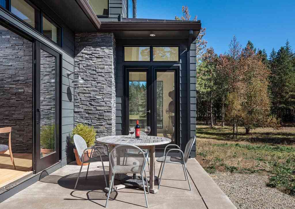 A stone wall in black house and table and chair outside of the house and tree