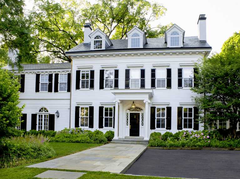White house with the black shutter and tree and plants outside the house