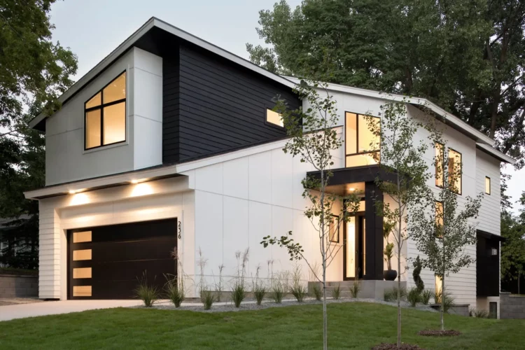White house with black trim and lights above the wall and wooden door and garden outside of the door