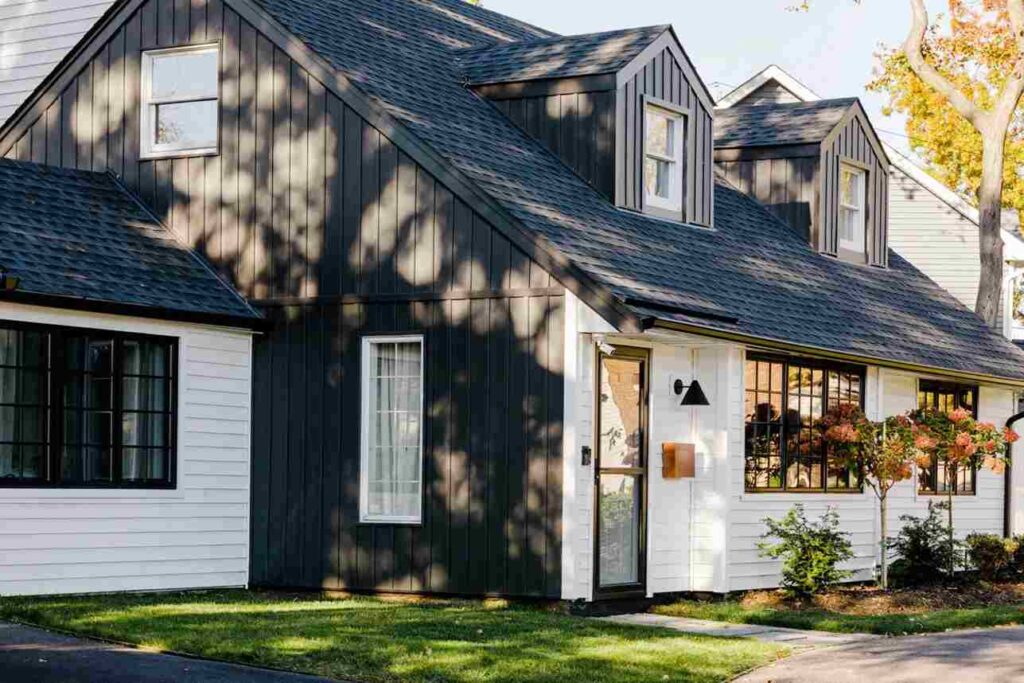 A white brick house and black siding and glass window and plants outside of the house