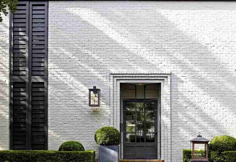 White brick wall and black glass door with plants and lights