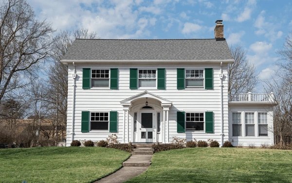 A gray and white house and white door and garden each side of the house