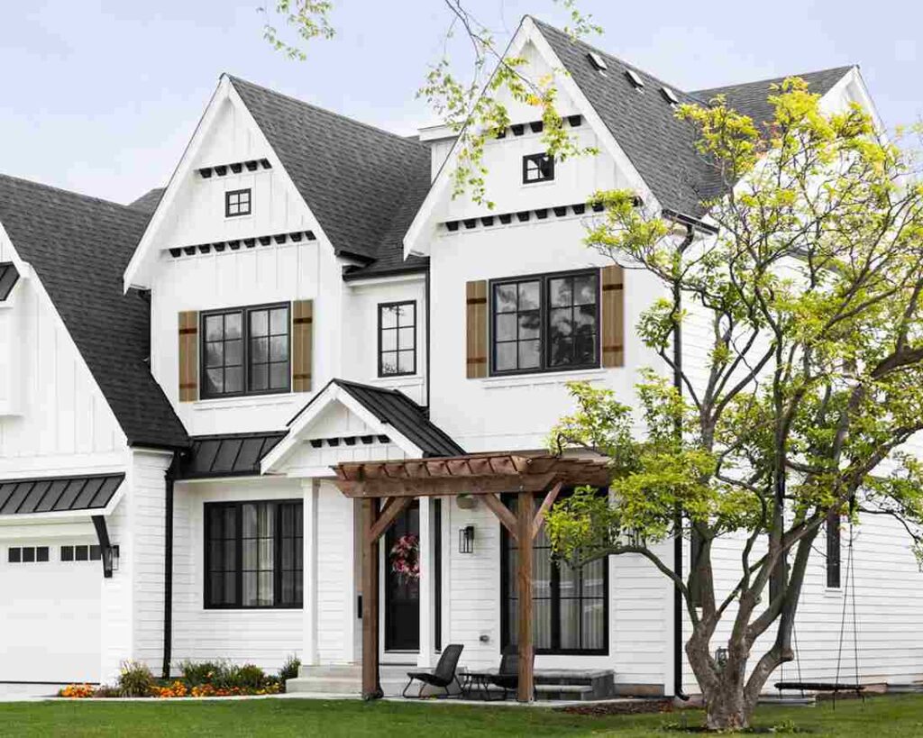 A white house and wooden shutter and black window and tree outside of the house and garden outside