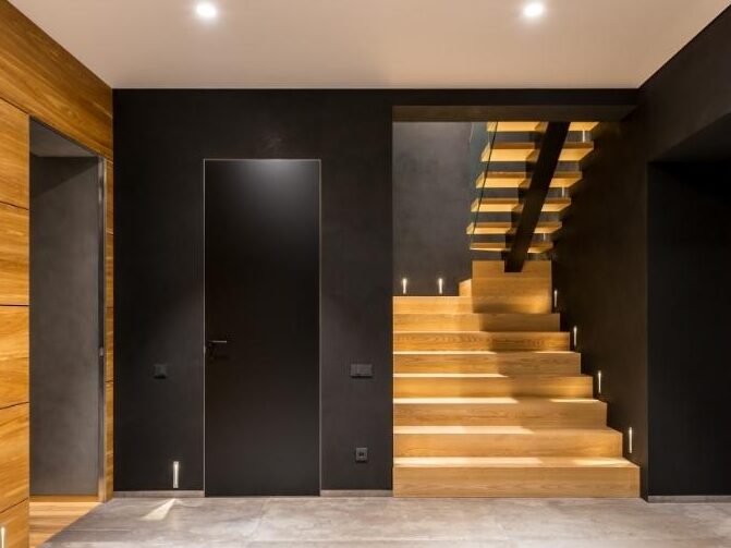 A wooden staircase with black wall and warm lights