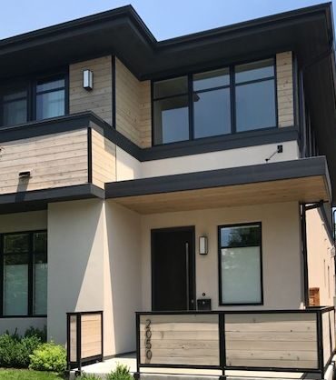 Tan house with black glass windows and black door and lights on the wall
