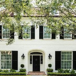 A white house with black shutter and   and windows and lights on the wall 