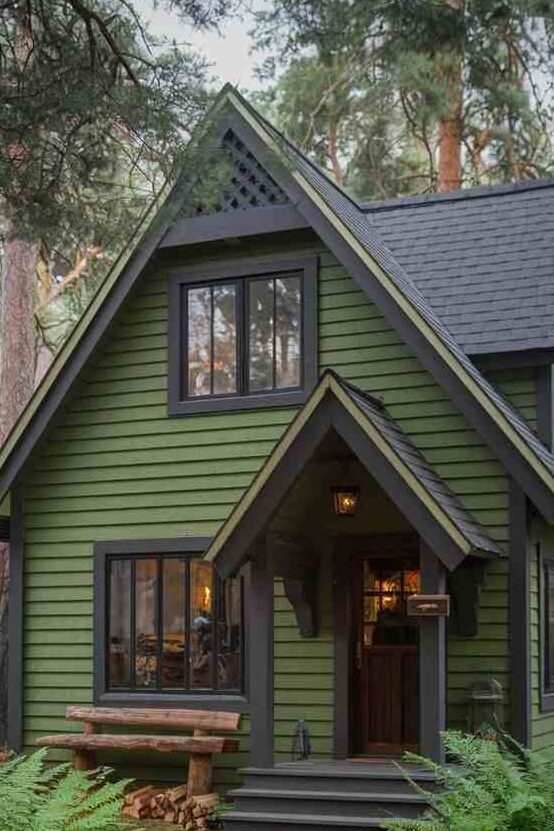 Dark green house with black framed windows and lights above the wall