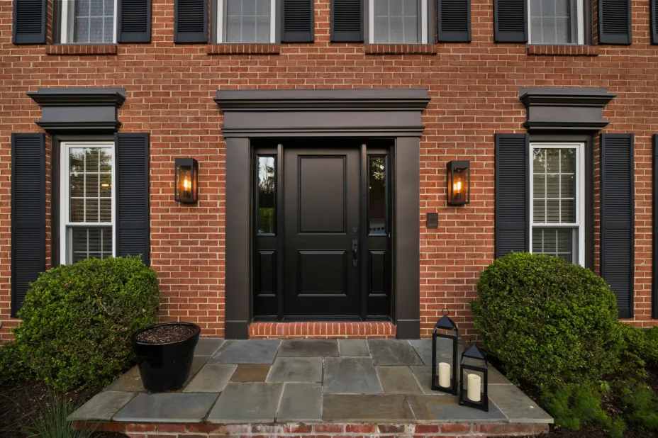 Black front door on red brick house exterior and lights on the wall with white trim windows