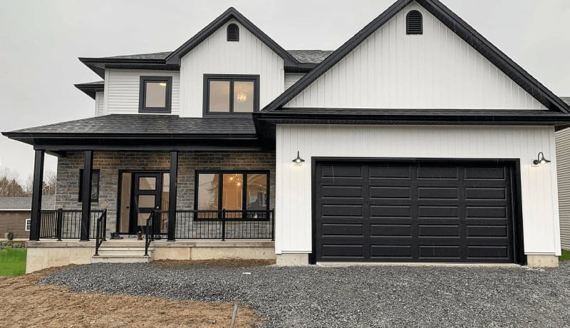 A white house with black garage door and windows and black roof