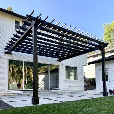 Black pergola on white brick house with glass windows 