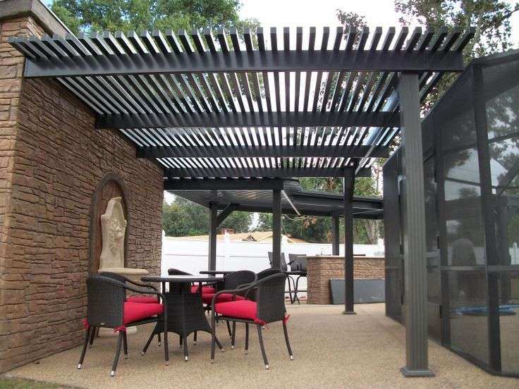 Black pergola with tan house and chairs and table outside of the house
