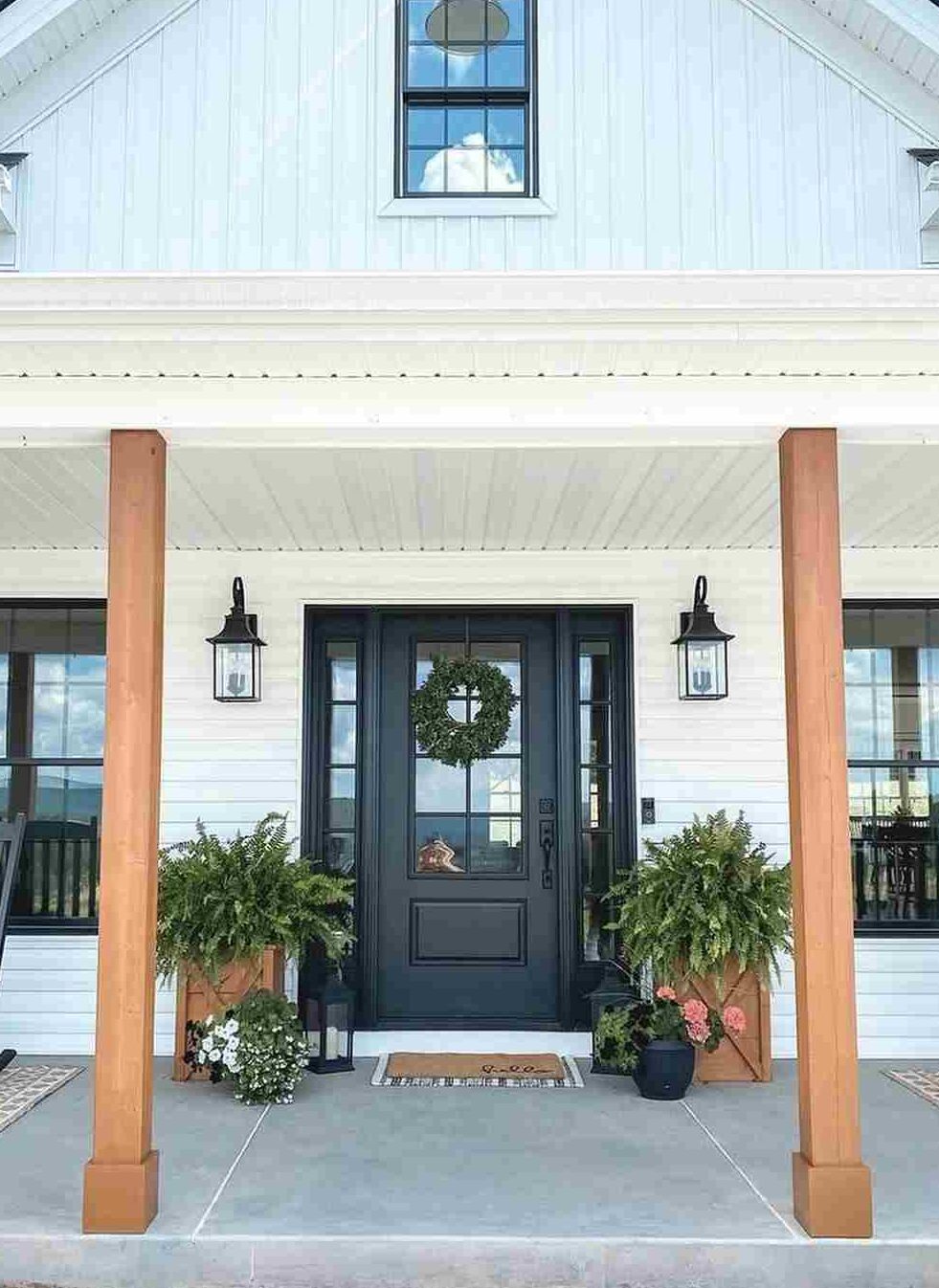 A white house with blak front door and flowers outside of the house