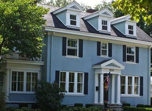 Blue house with black shutter and white windows and pillar and garden outside of the house