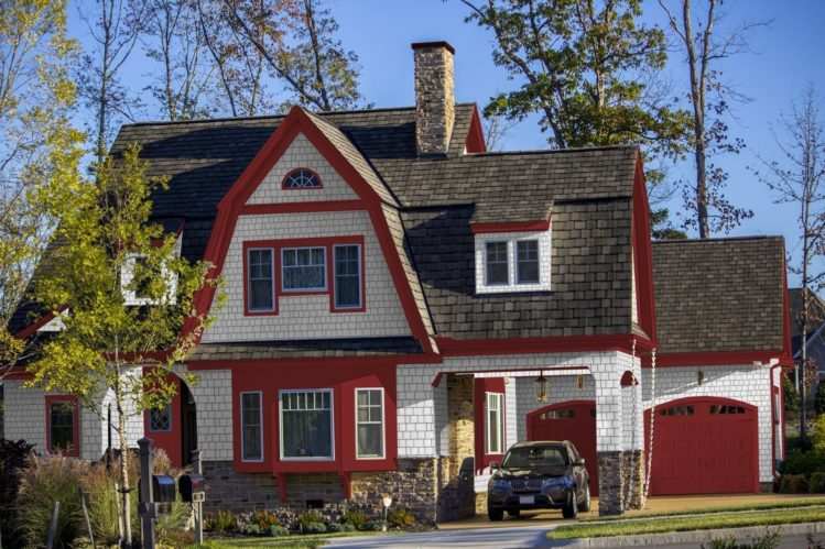 Brown roof on white house with red trim and car outside of the house 