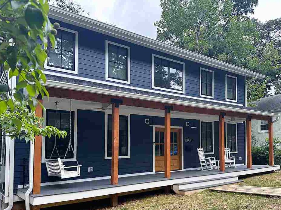 Cedar beams on dark blue house and white trim windows and chairs outside of the house