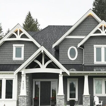 A grey house with white trim and white pillars on stone base and lack front door 