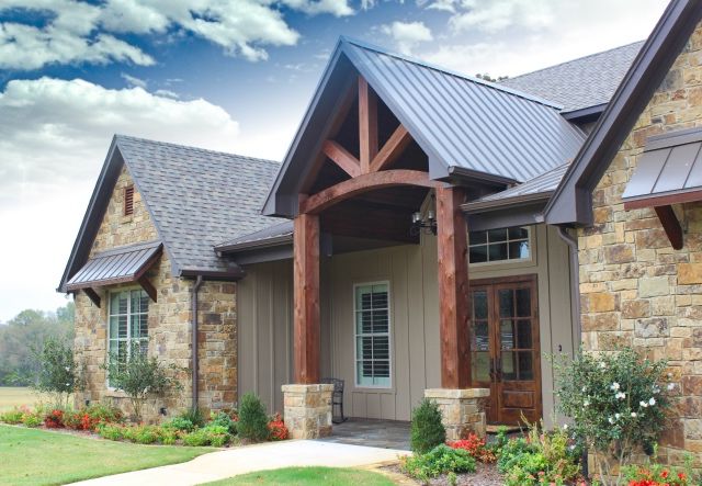 A stone house with black roof and wooden accents and white trim windows 
