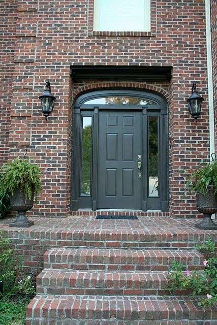 Brown brick house with black door and brick stairs and lights on the wall