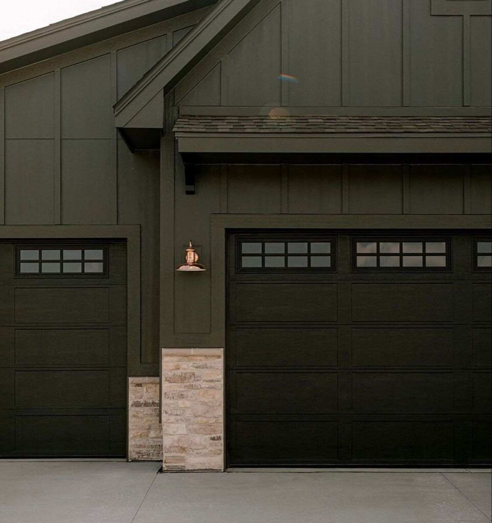 A deep green house with black garage door 