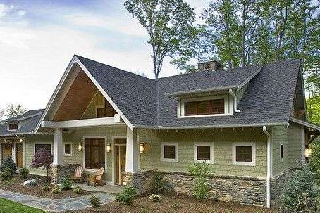 Sage green house with stone base and black roof and white trim and lights above the wall
