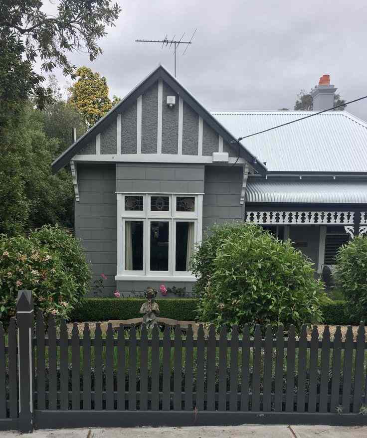 A grey house with black fencing around the house and white windows 
