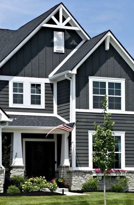 A grey house with white windows and stone base garden outside of the house 