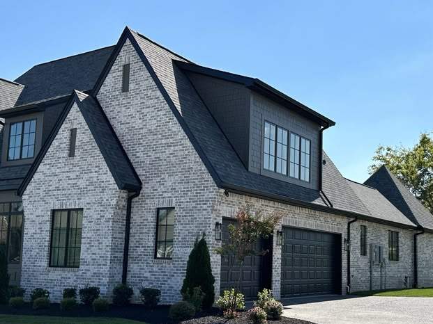 Stone house with black roof and wooden garage door and black trim windows 