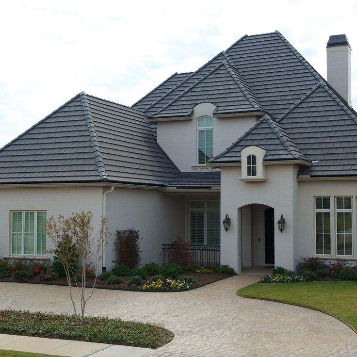 A grey house with black roof and white frame window and lights on the wall and a pathway
