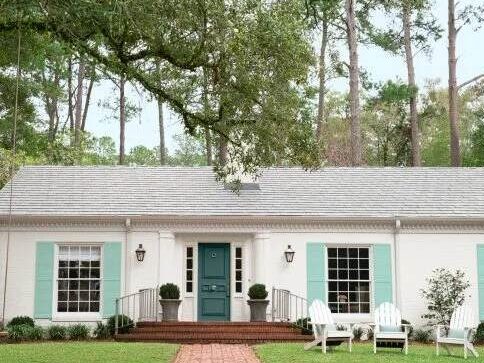 White house with green door and and blue shutters and garden outside of the house