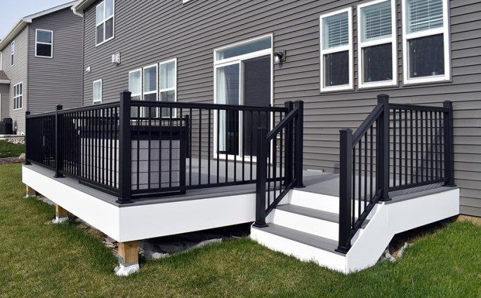 A grey house with black railing and white trim windows