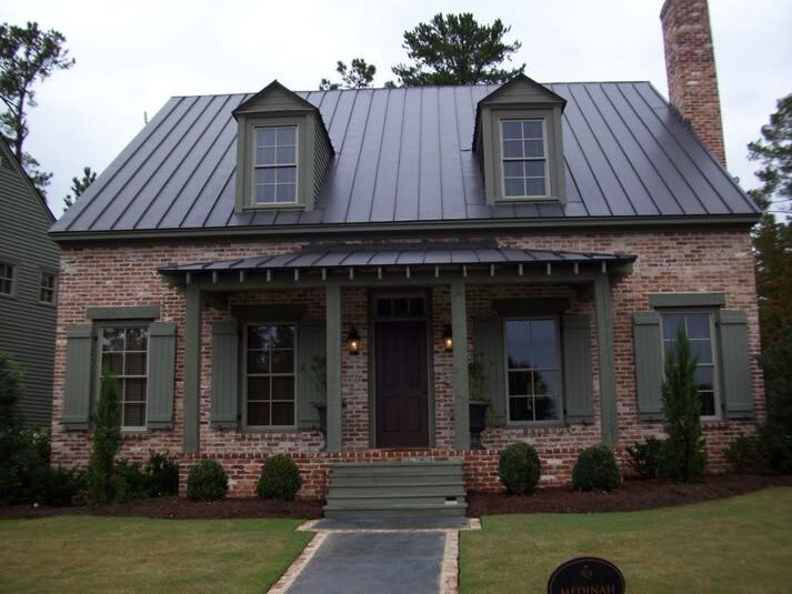 Tan brick house with metal cladding roof and garden outside of the house and lights on the wall
