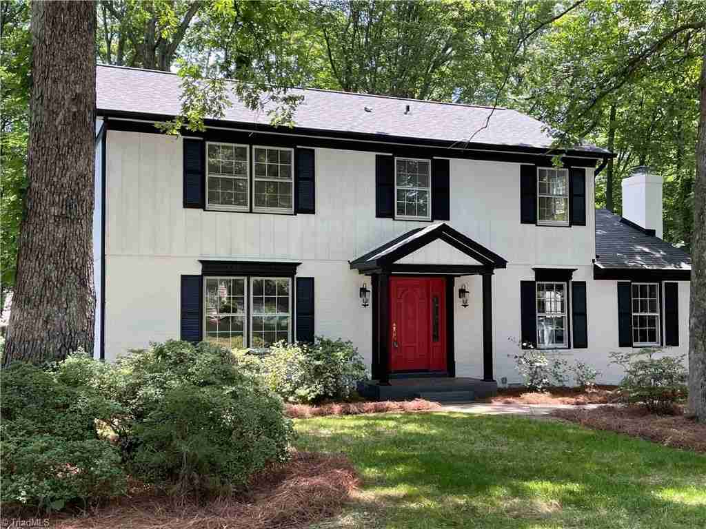 Lush greenery white house with red door and glass windows 
