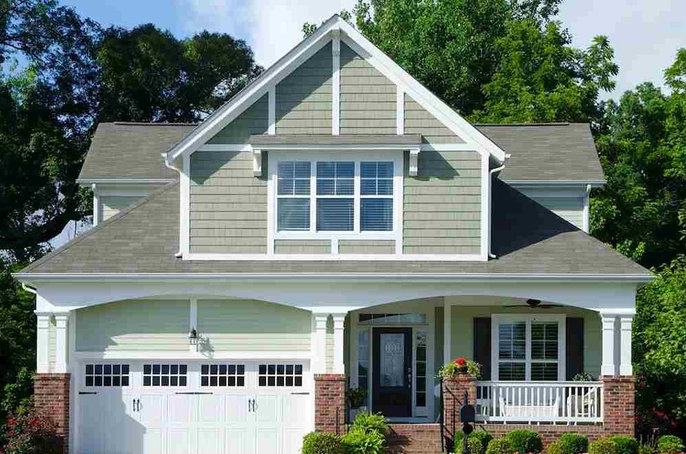 Sage house with white garage door and white framed windows and black door