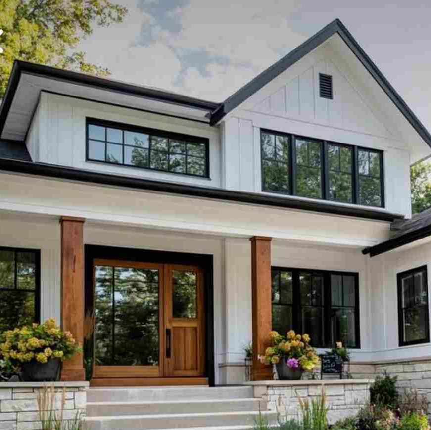 A white house with black trim and wooden pillars and wooden door