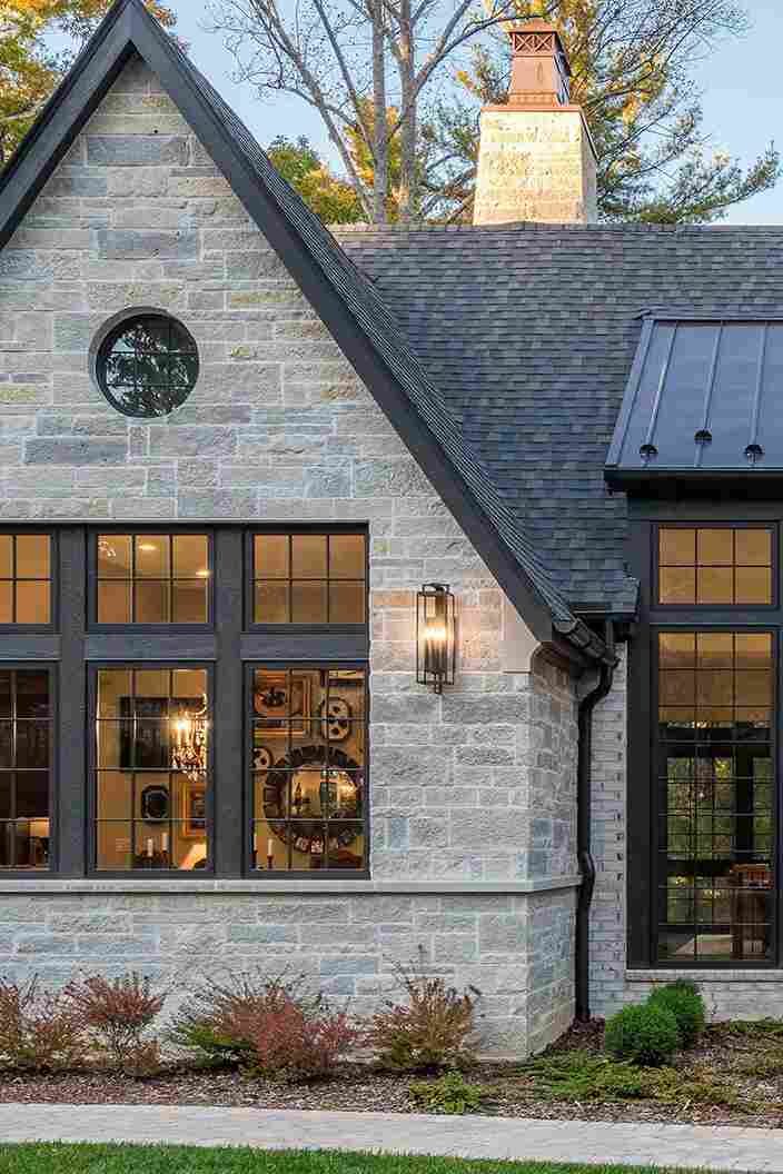 A stone house with wooden trim windows ad black roof 