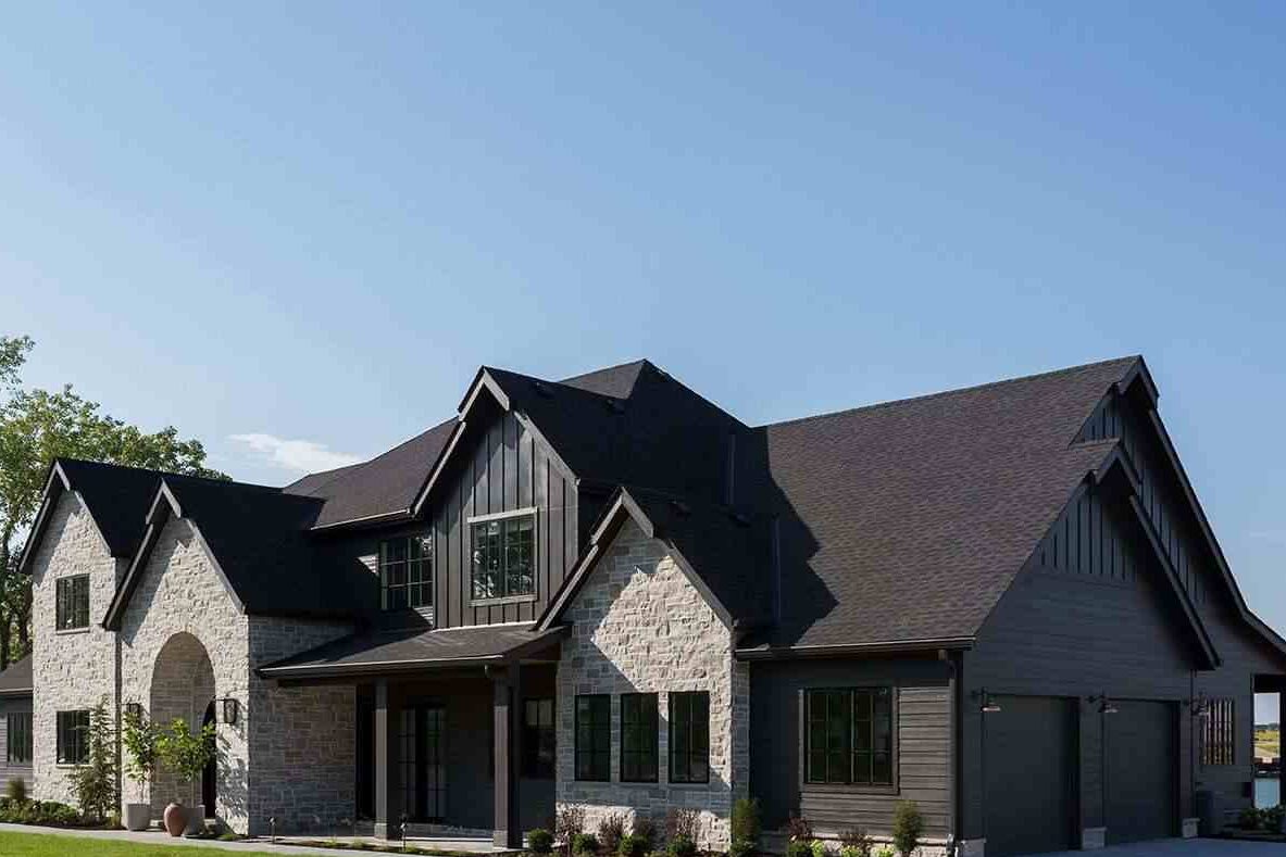 Pale grey stone with black roof and windows and garden outside of the house 